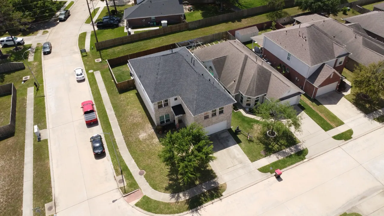Wide aerial view of a two-story home with a dark shingle roof on a corner lot