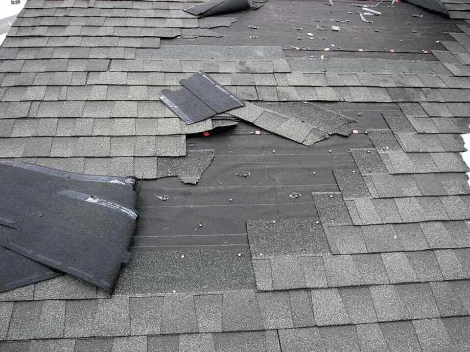 Roof with missing and displaced shingles exposing the underlayment
