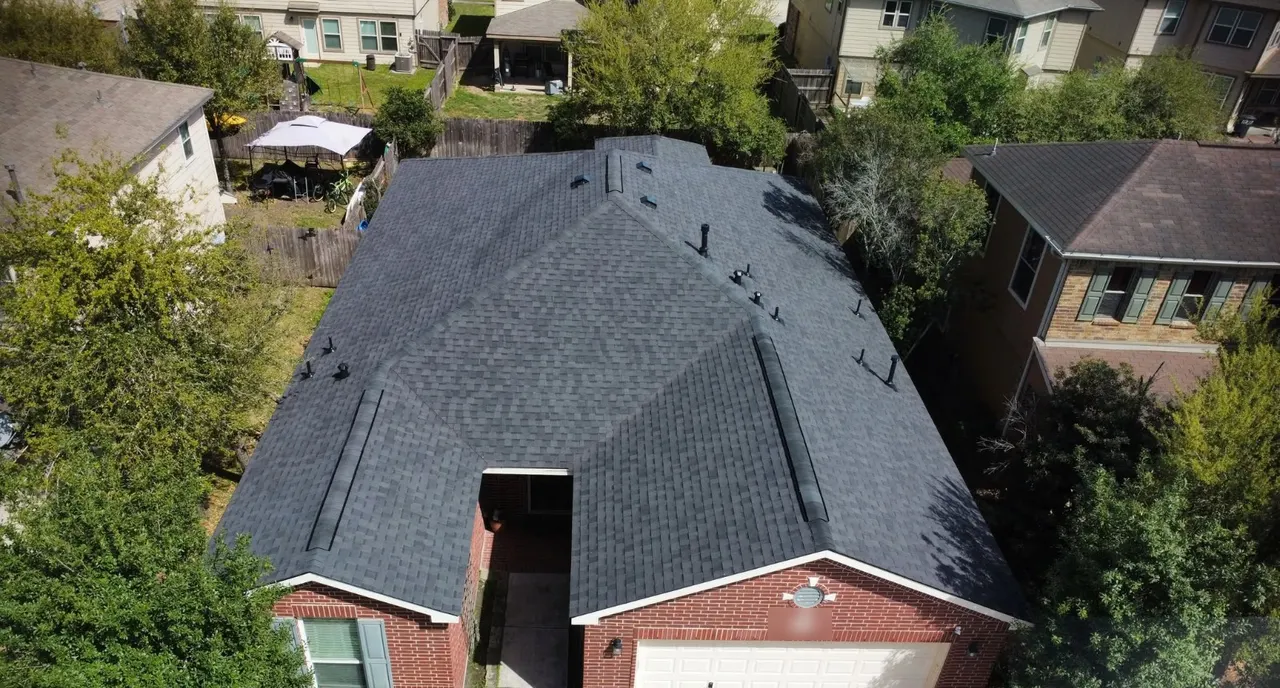 Overhead view of a dark shingle roof with ridge vents on a red-brick home
